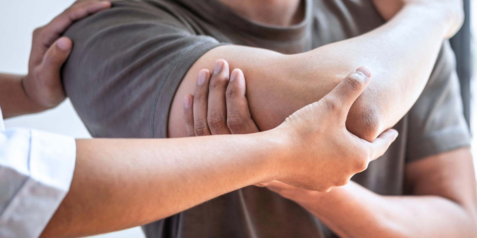 This is an image of a clinician examining a patient's right arm, holding their shoulder and elbow.