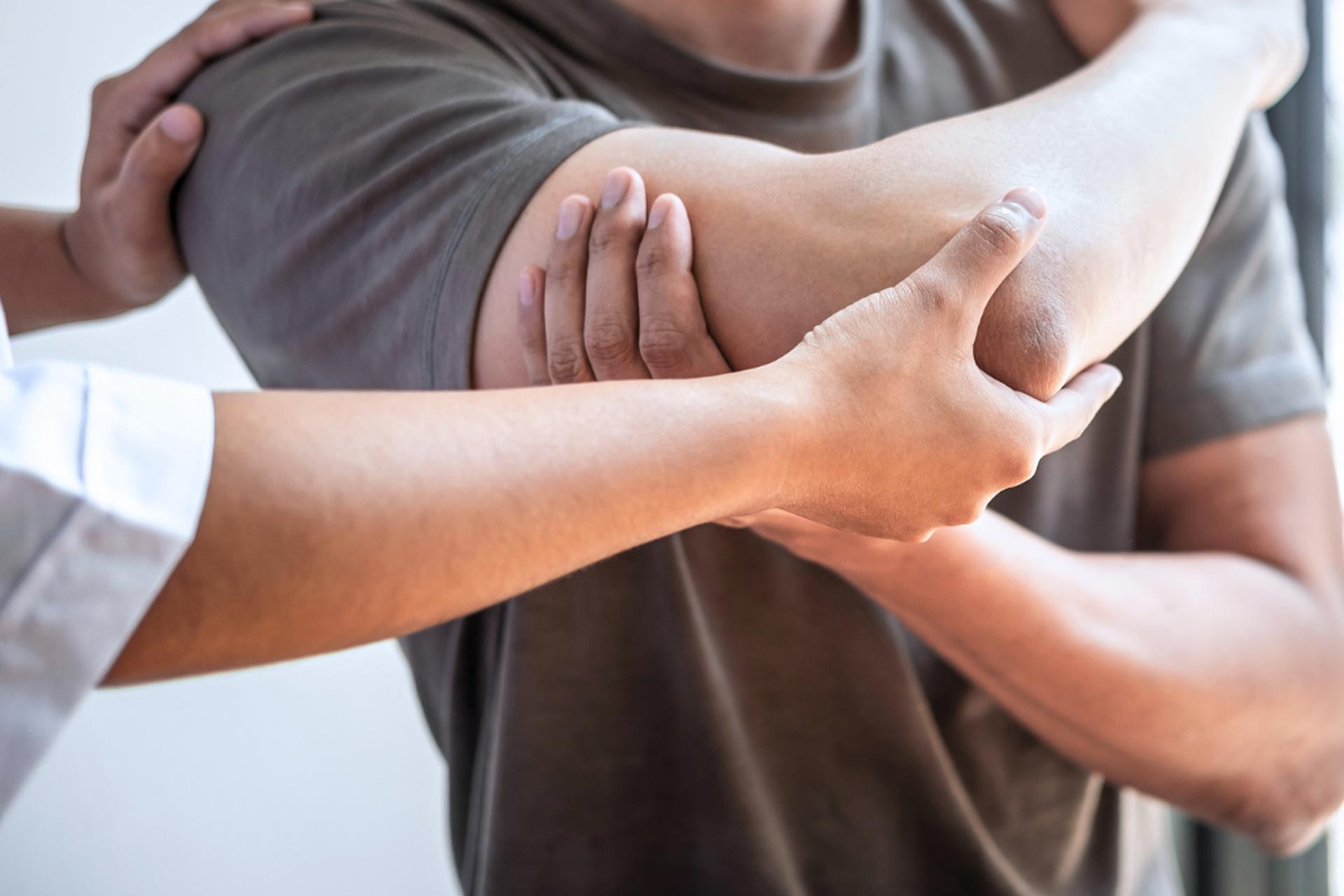 This is an image of a clinician examining a patient's right arm, holding their shoulder and elbow.