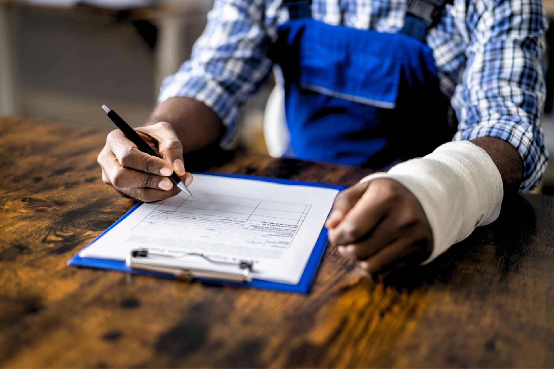 This is an image of a man filling out worker's compensation forms on a clipboard. He has a bandage on his left hand.