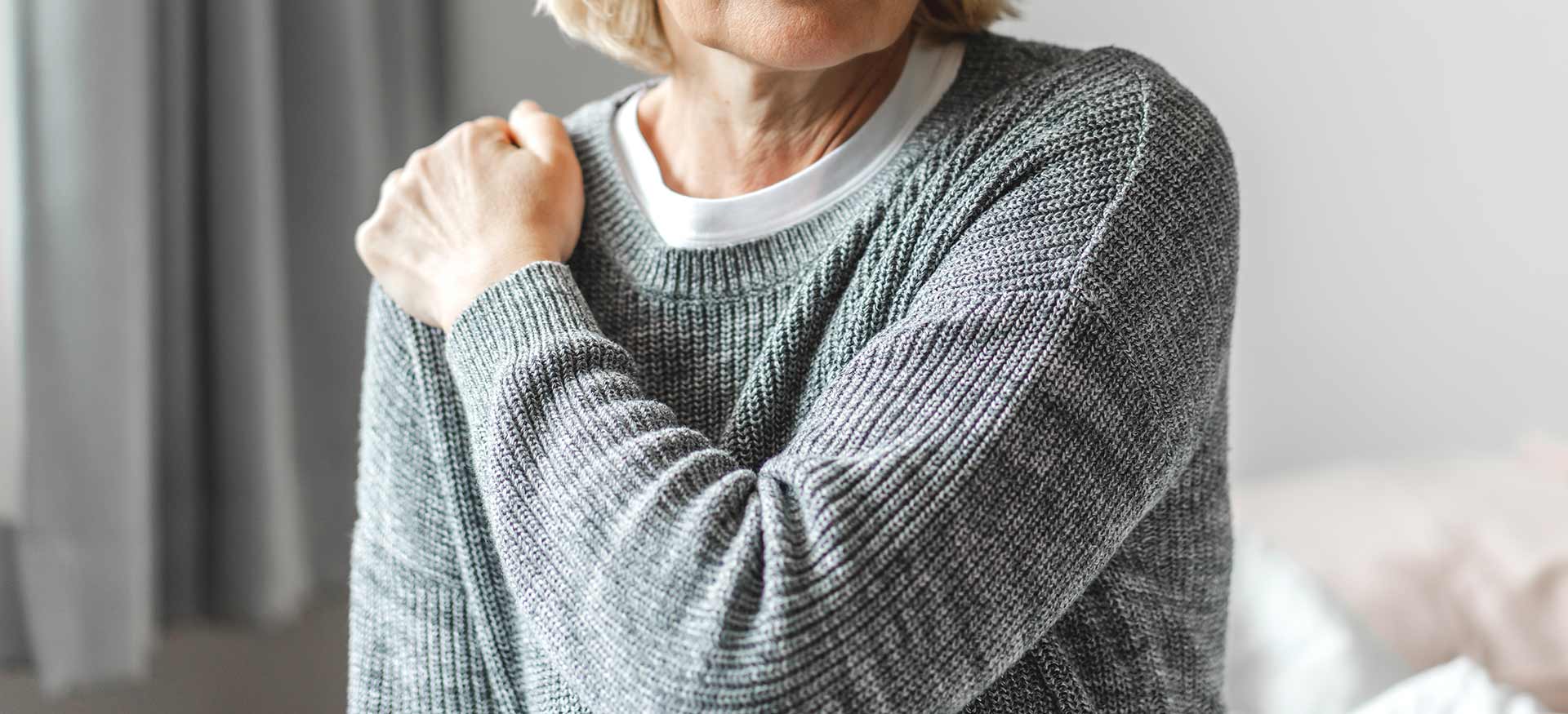 This is an image of an older woman holding her right shoulder, indicating right shoulder pain or injury.