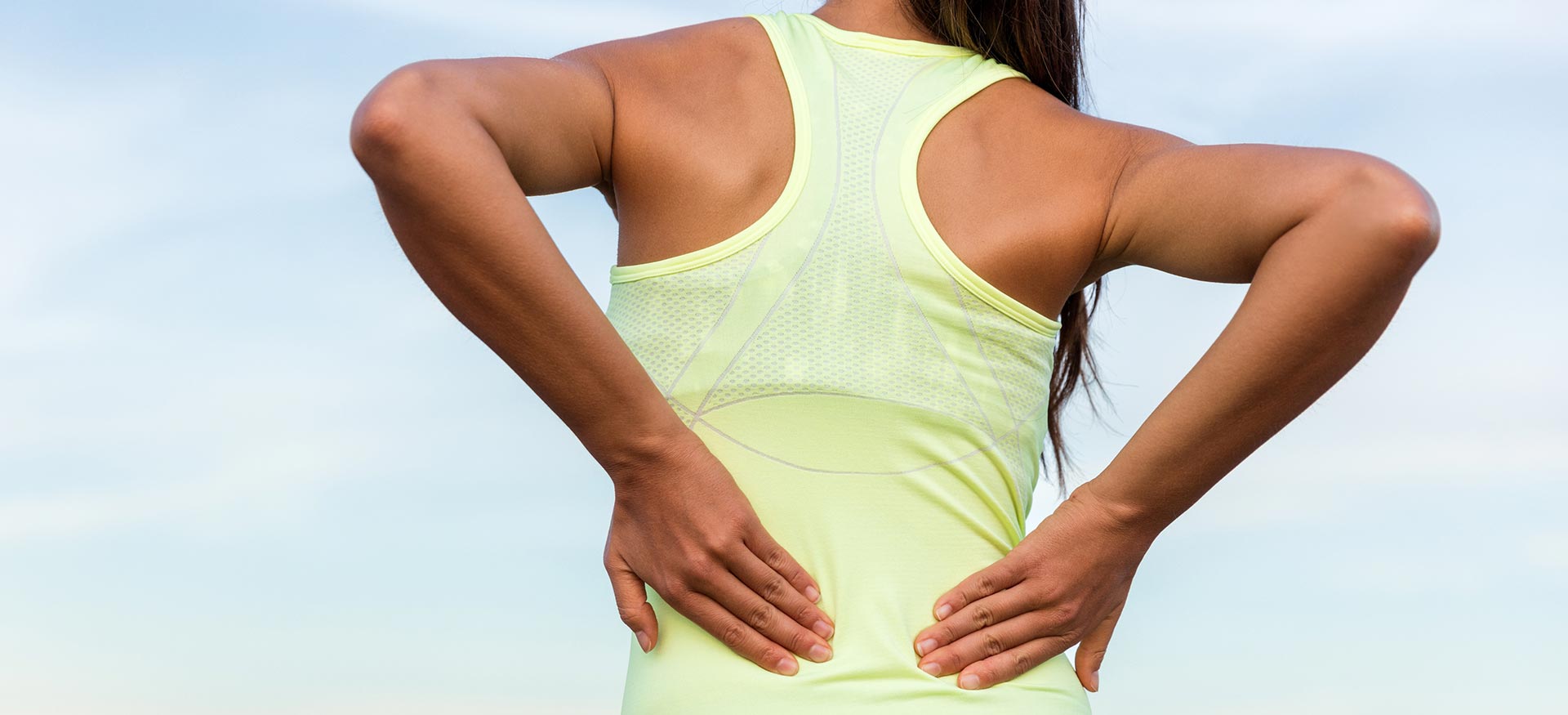 This is an image of an young athletic woman holding her lower back, indicating lower back pain or injury.